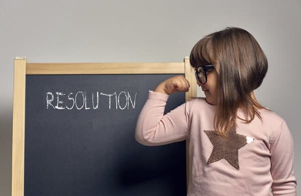 A young child flexes an arm next to a blackboard that says "Resolution"