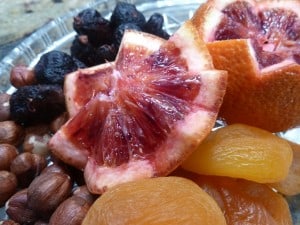 A photograph that is a close-up of a pile of dried fruit. On the top is a blood orange cut into a star.