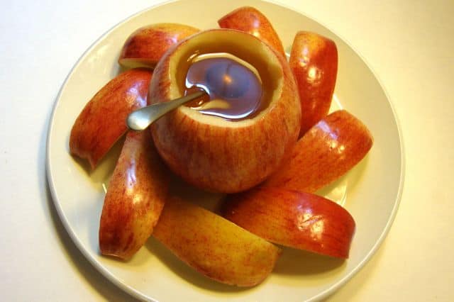 Red apple slices surrounding a cup of sweet honey.