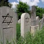 A photograph of a row of headstones in a graveyard, each with a Star of David engraved into it.