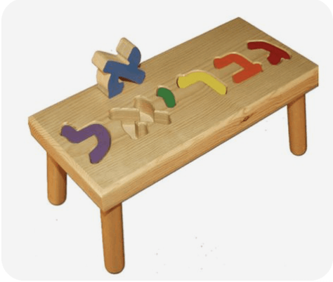 A screenshot of a wooden baby toy. It's a small table with puzzle pieces forming the name Gabriel in Hebrew. Each letter is a different color. The aleph, blue, is lifted out of its puzzle slot.