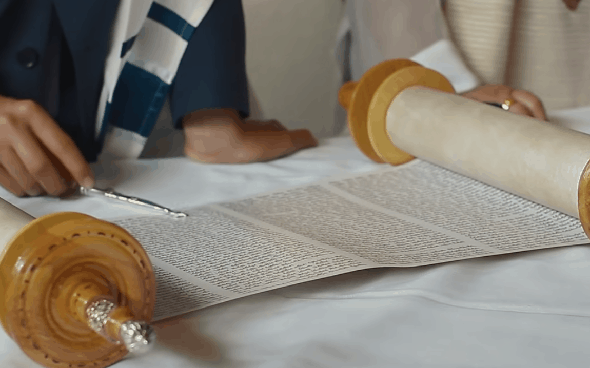 Screenshot of two people reading from a small Torah.