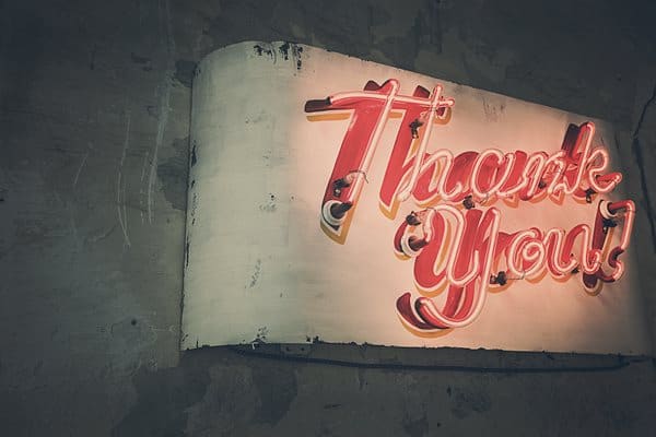 A photo of a nondescript wall that has a giant neon sign that says Thank you!