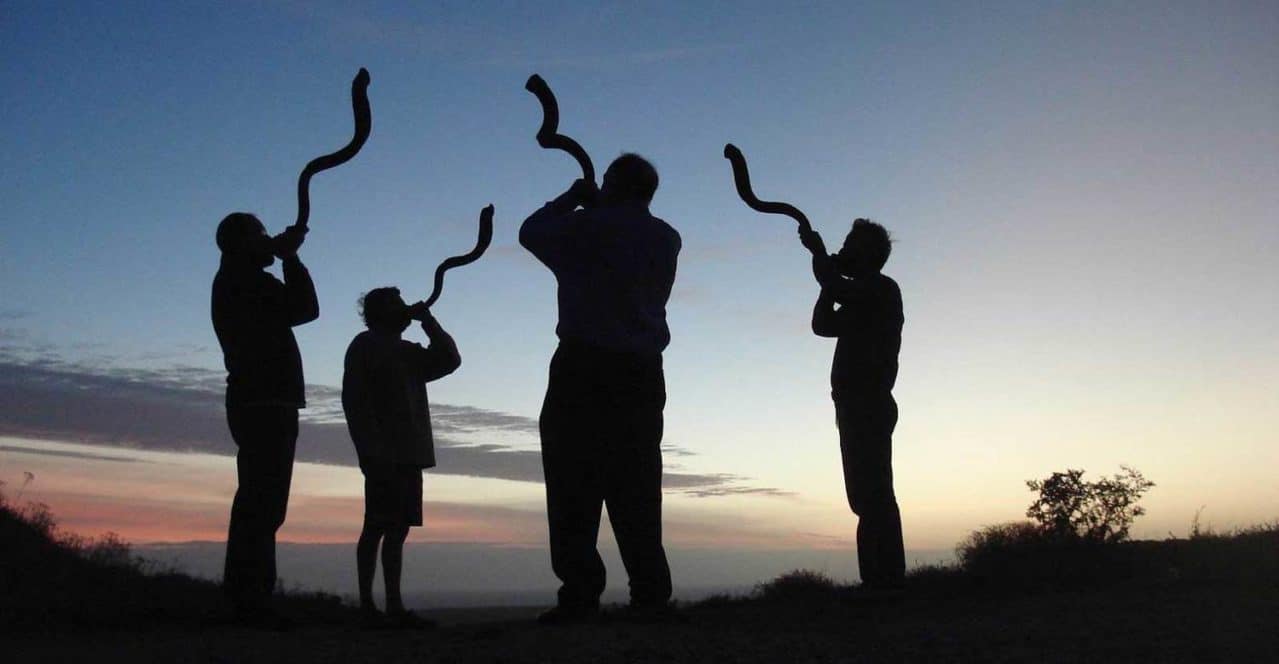 A photograph of four people blowing shofars during sunrise.