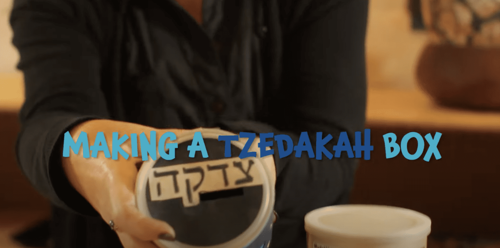 A screenshot of a youtube video of someone holding a tzedakah box.