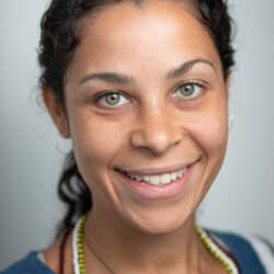 A headshot of Sarah Kolker. She is a Black woman with her hair tied into a ponytail and wearing a teal top.