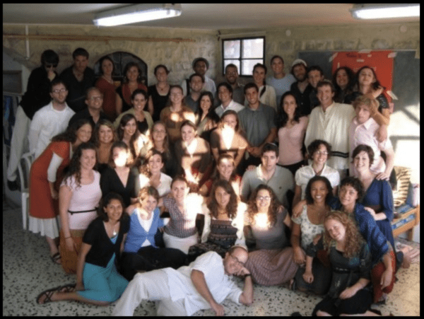 A photograph of about 30 teens and young adults posing together inside a nondescript room with sunlight spilling across their faces.