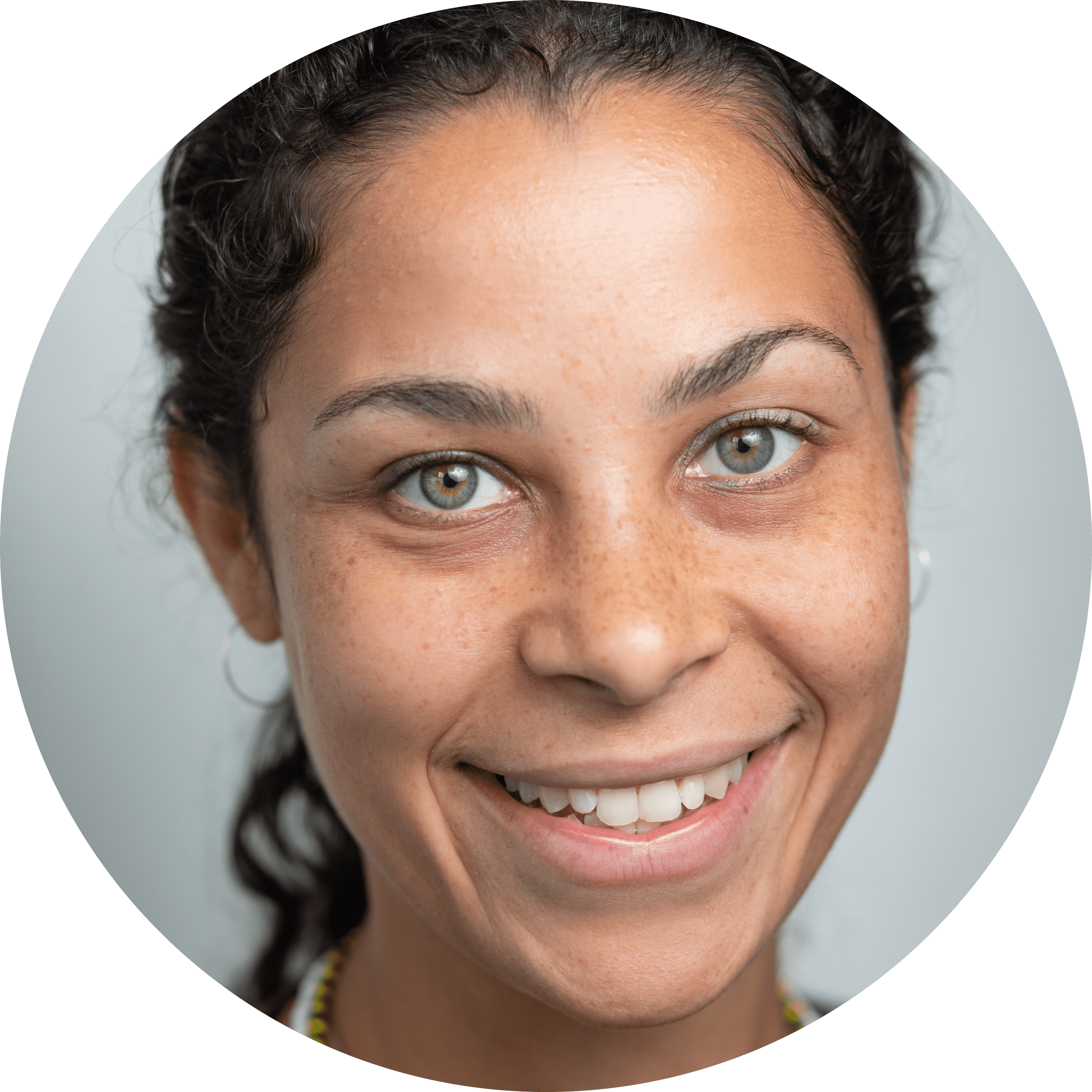 A close-up headshot of a Black woman with freckles, green eyes, hair in a ponytail, and a wide smile.