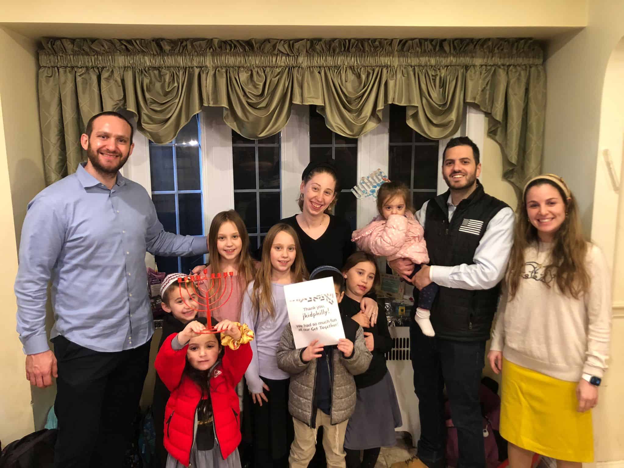 A photo of several adults and children standing and smiling together, with a sign that says thank you jkidphilly we had so much fun at our get together