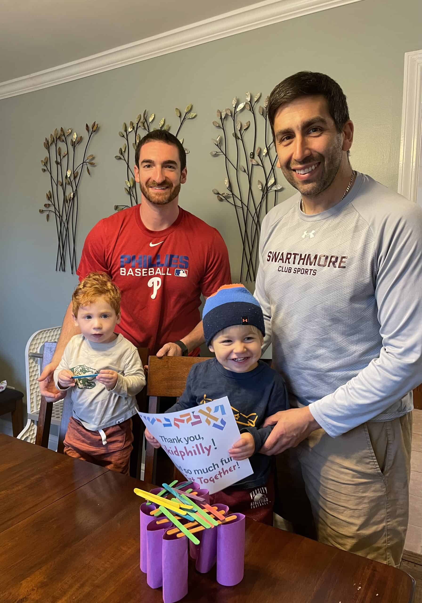 A photo of two adults and two toddlers smiling and holding a sign that says thank you jkidphilly we had so much fun at our get together