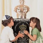 a photo of two children kissing either side of a large, ornate dressed Torah