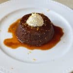 A photo of one chocolate flan on a plate smothered in sauce.