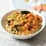 A bowl of couscous with cucumbers, chickpeas, carrots, and other vegetables on top.